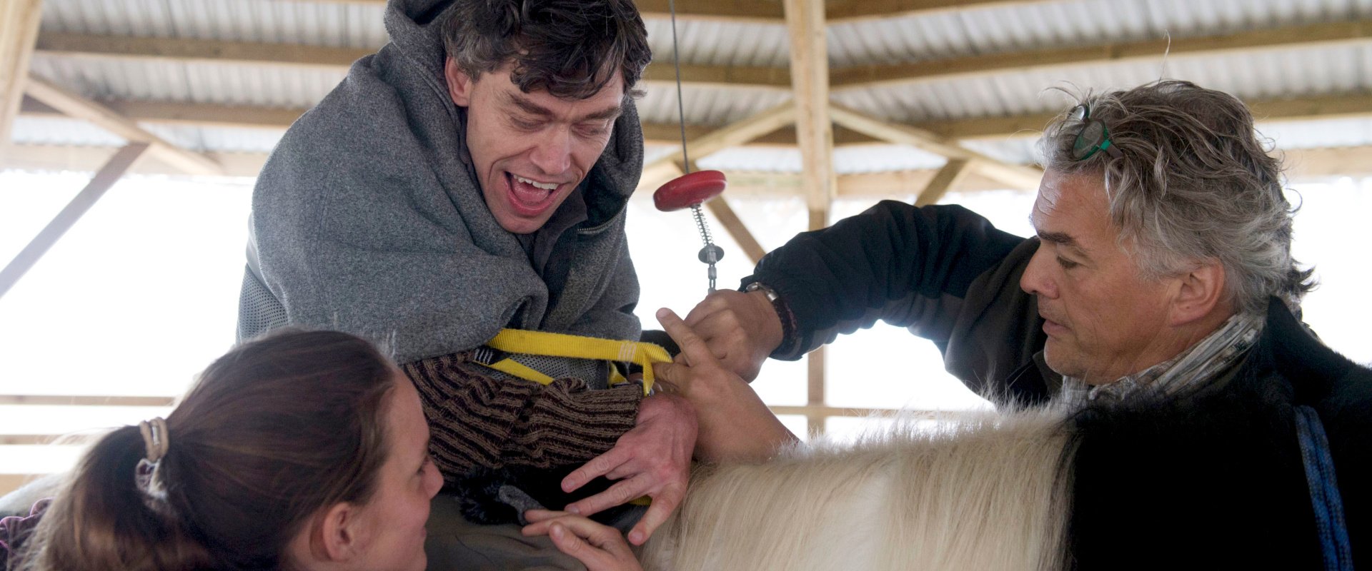 une personne polyhandicapée sur un cheval, aidée par un élévateur et deux hippothérapeutes